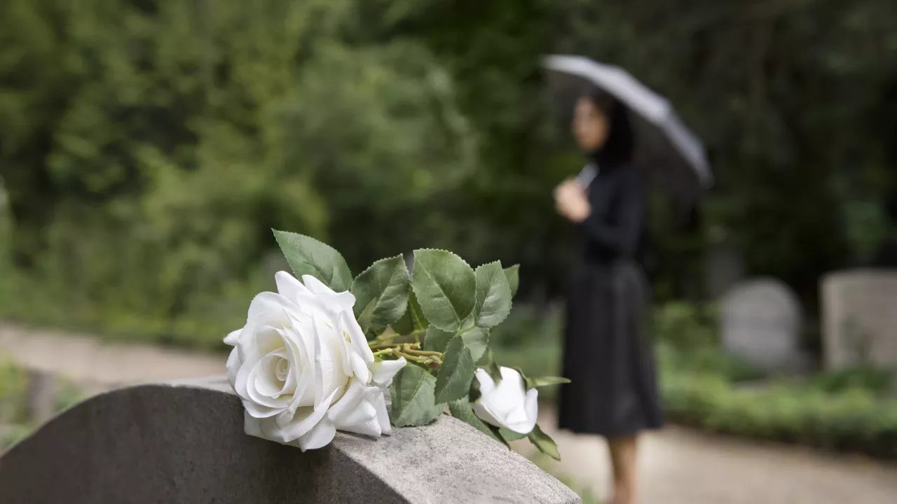 Rose blanche sur une pierre tombale avec femme en deuil en arrière-plan.