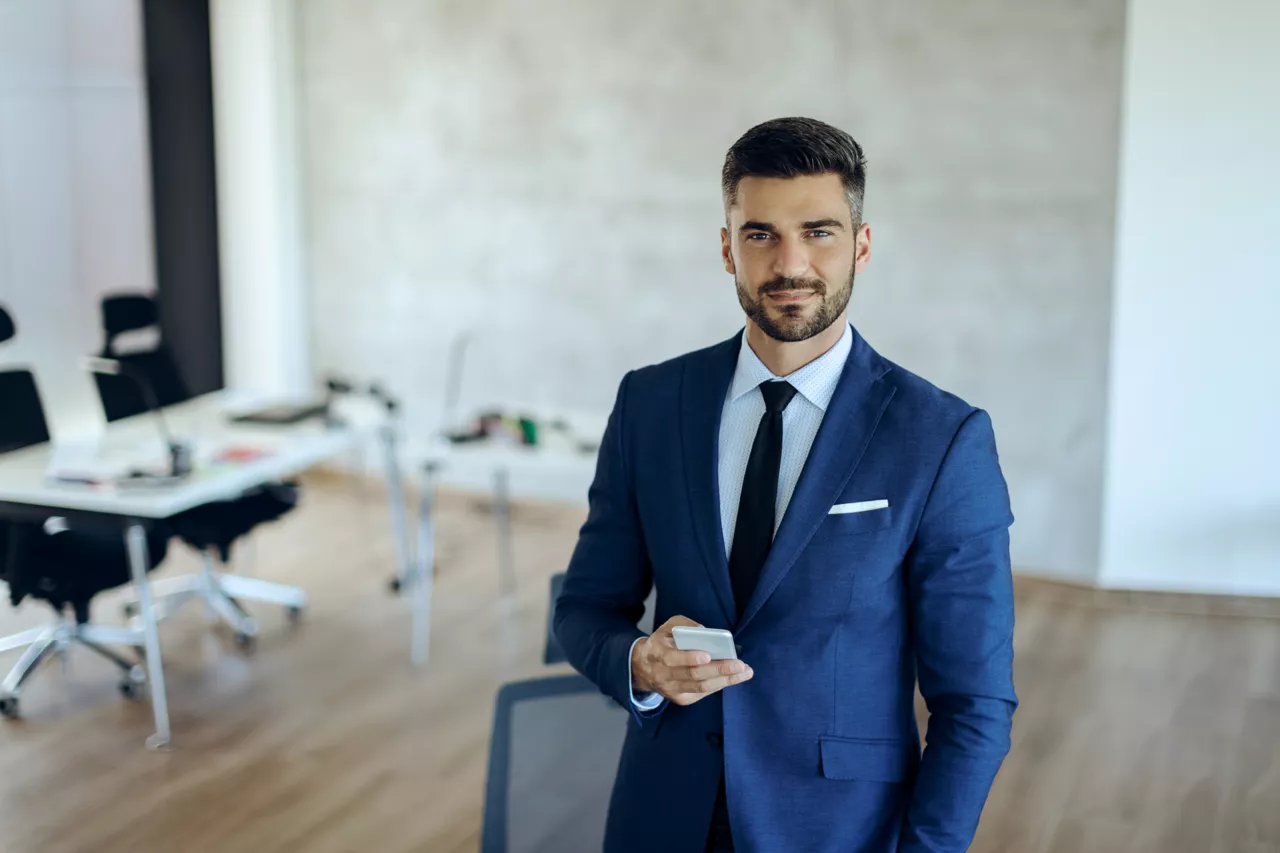 Homme d'affaires sérieux tenant un téléphone mobile dans un bureau moderne.