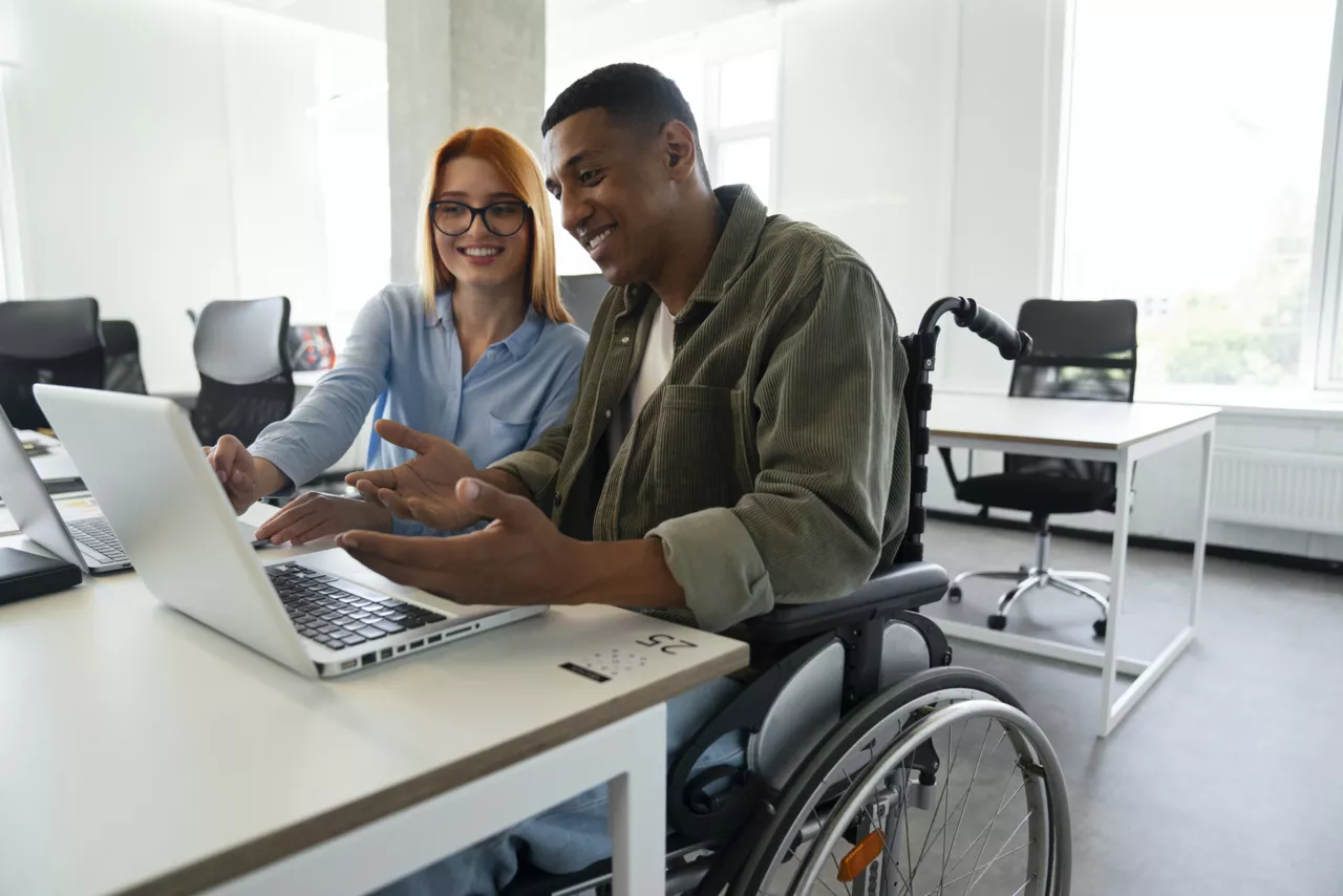 Deux collègues, un homme en fauteuil roulant et une femme, travaillant ensemble sur un ordinateur portable.